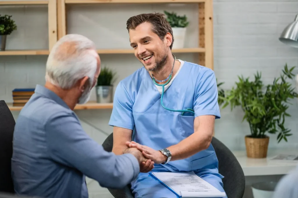 happy gp talking to senior man shaking hands in hospital